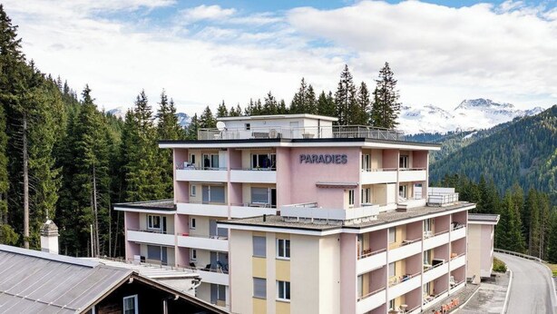 A multi-story hotel named 'PARADIES' with balconies, a parking area, and a mountainous backdrop. - Paradies 001 Appartement/Fewo, Bad, WC, 6-Bettwohnung 6-Bettwohnung by Interhome (Arosa)