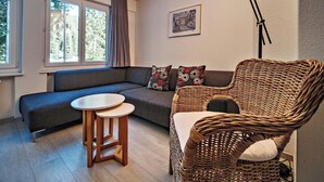 A cozy living room with a sofa, a wicker chair, a small table, and a floor lamp. - Paradies 001 Appartement/Fewo, Bad, WC, 6-Bettwohnung 6-Bettwohnung by Interhome (Arosa)