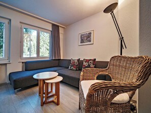 Ein gemütliches Wohnzimmer mit einer Couch, einem Korbsessel, einem kleinen Tisch und einer Stehlampe.