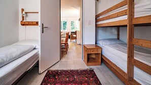 A compact room with two bunk beds, a small bedside table, a chair, and a dining area with a table and chairs. - Paradies 001 Appartement/Fewo, Bad, WC, 6-Bettwohnung 6-Bettwohnung by Interhome (Arosa)