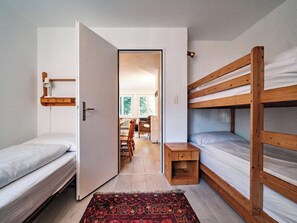 Ein gemütlicher Raum mit zwei Etagenbetten, einem kleinen Nachttisch, einem Stuhl und einer Essecke mit Tisch und Stühlen.