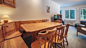 A dining area with a wooden table and chairs, a television, and a window with a view of trees. - Paradies 001 Appartement/Fewo, Bad, WC, 6-Bettwohnung 6-Bettwohnung by Interhome (Arosa)