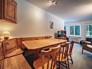 Ein Essbereich mit Holztisch und Stühlen, einem Fernseher und einem Fenster mit Blick auf Bäume.
