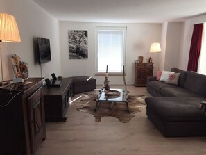 A living room with a sofa, a coffee table, a lamp, a television, and a window with blinds. - Alkazar Wg. 11 Appartement/Fewo, Bad, WC, 6-Bettwohnung by Interhome (Arosa)