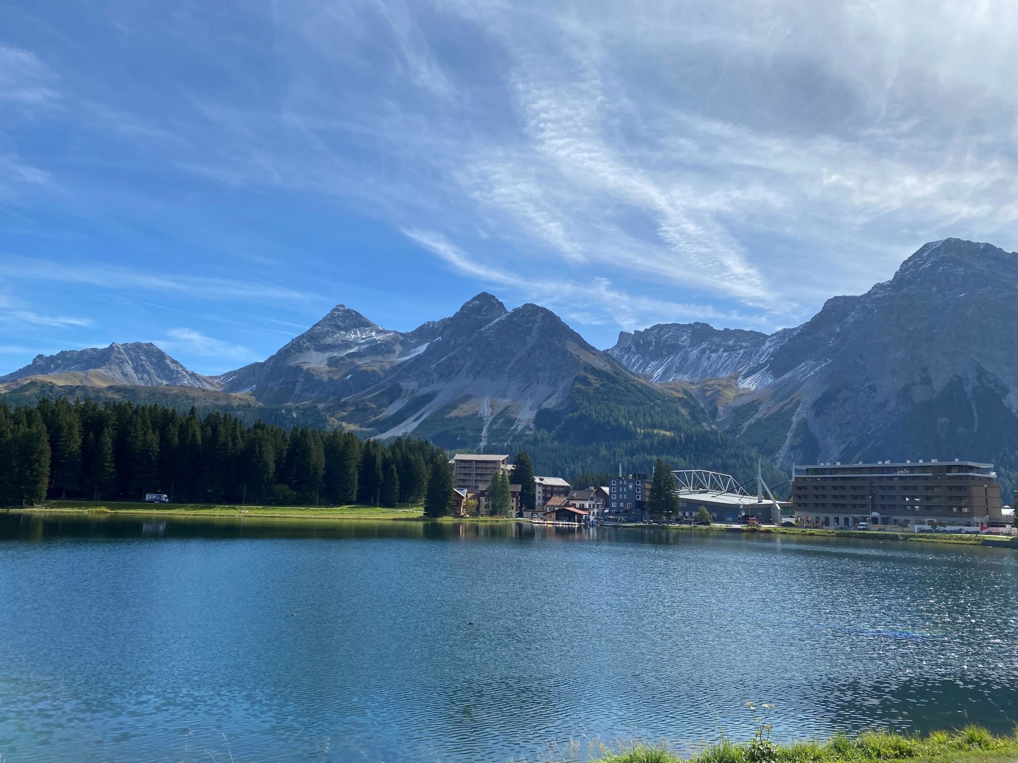 A lake with mountains in the background, a building with a bridge, and a forested area.