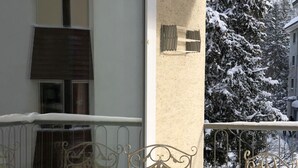 Metallstolar och ett bord utomhus på en balkong, med snötäckta träd i bakgrunden.