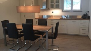 Ett modernt kök med ett matbord och stolar, vita skåp och ett fönster med persienner.