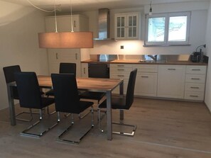 Eine moderne Küche mit Esstisch und Stühlen, weißen Schränken und einem Fenster mit Jalousien.