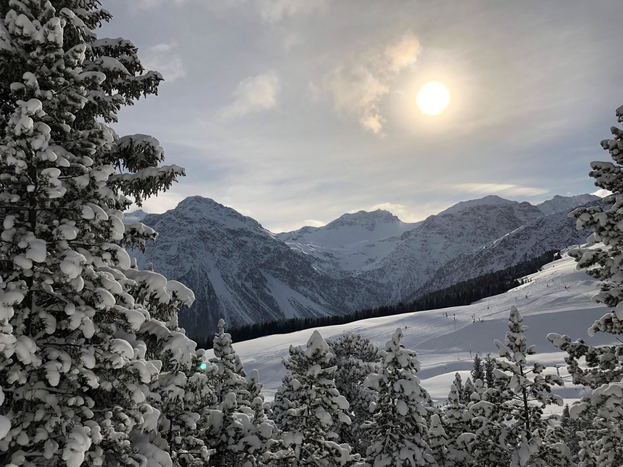A snowy mountain landscape with a clear sky and the sun visible.