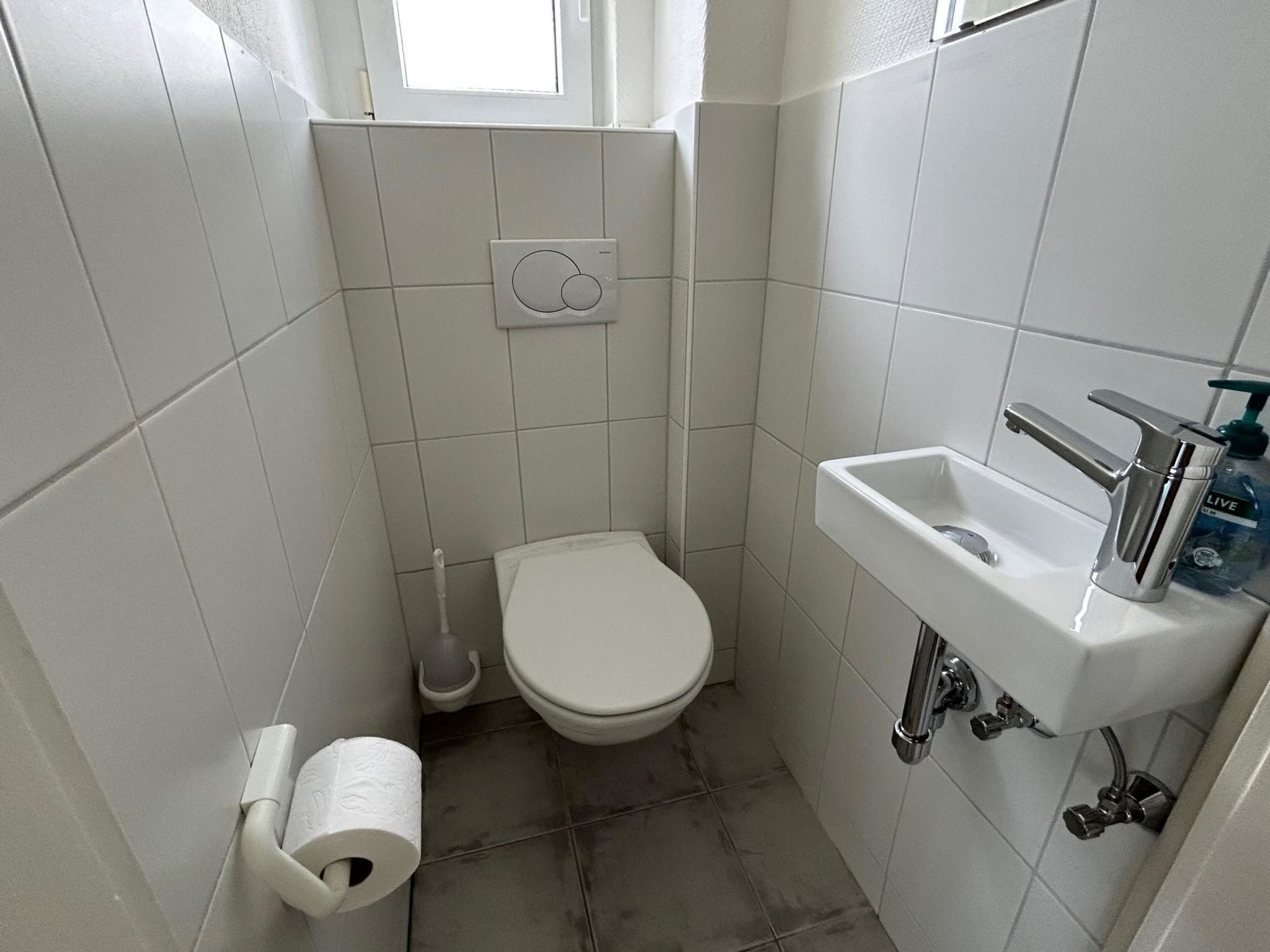 Ett litet badrum med kakel på väggarna, utrustat med en toalett, ett handfat och en hållare för toalettpapper.