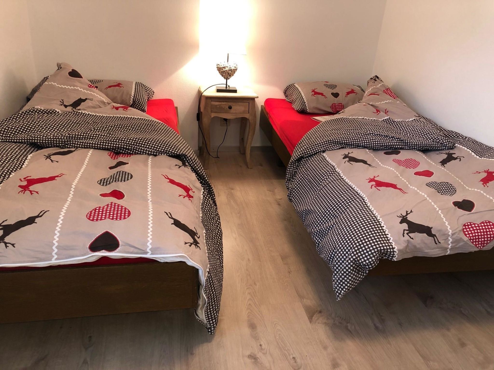 Habitación con dos camas, cada una con ropa de cama y almohadas estampadas, una mesita de noche pequeña con lámpara y suelo de madera.