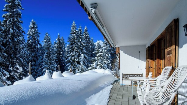 Een besneeuwd landschap met een gebouw, voorzien van een terras met buitenmeubilair.