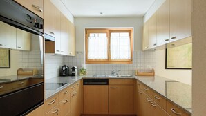 Een kleine keuken met houten kastjes, een inbouwoven en een raam met gordijnen.