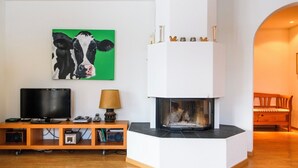 Een moderne woonkamer met een open haard, een televisie en een schilderij van een koe.