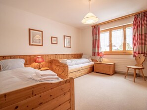 Ein Schlafzimmer mit zwei Holzbett, einem Nachttisch, einem Sessel, einem Fenster mit Vorhängen und Wandbildern.