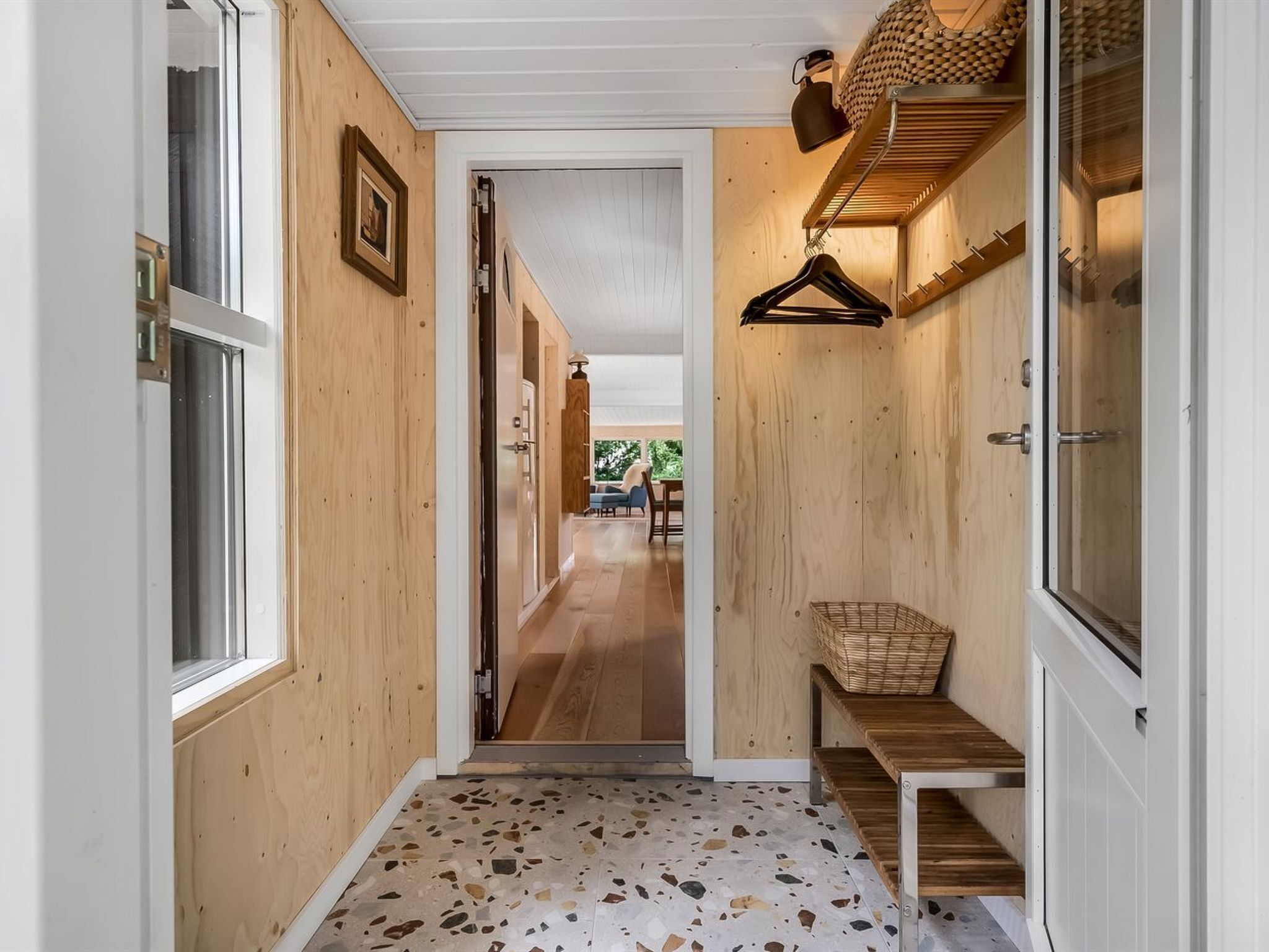 A hallway with wooden walls, a terrazzo floor, a hanging basket, and a bench.