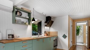 A modern kitchen with teal cabinets, a wooden countertop, a coffee maker, and a window overlooking a car. - "Hejne" - 600m from the sea by Interhome (Glesborg)