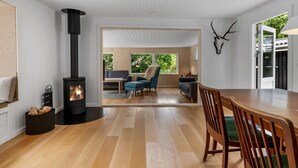A modern interior with a wood-burning stove, a dining area with a wooden table and chairs, and a view through a glass door to an outdoor seating area. - "Hejne" - 600m from the sea by Interhome (Glesborg)