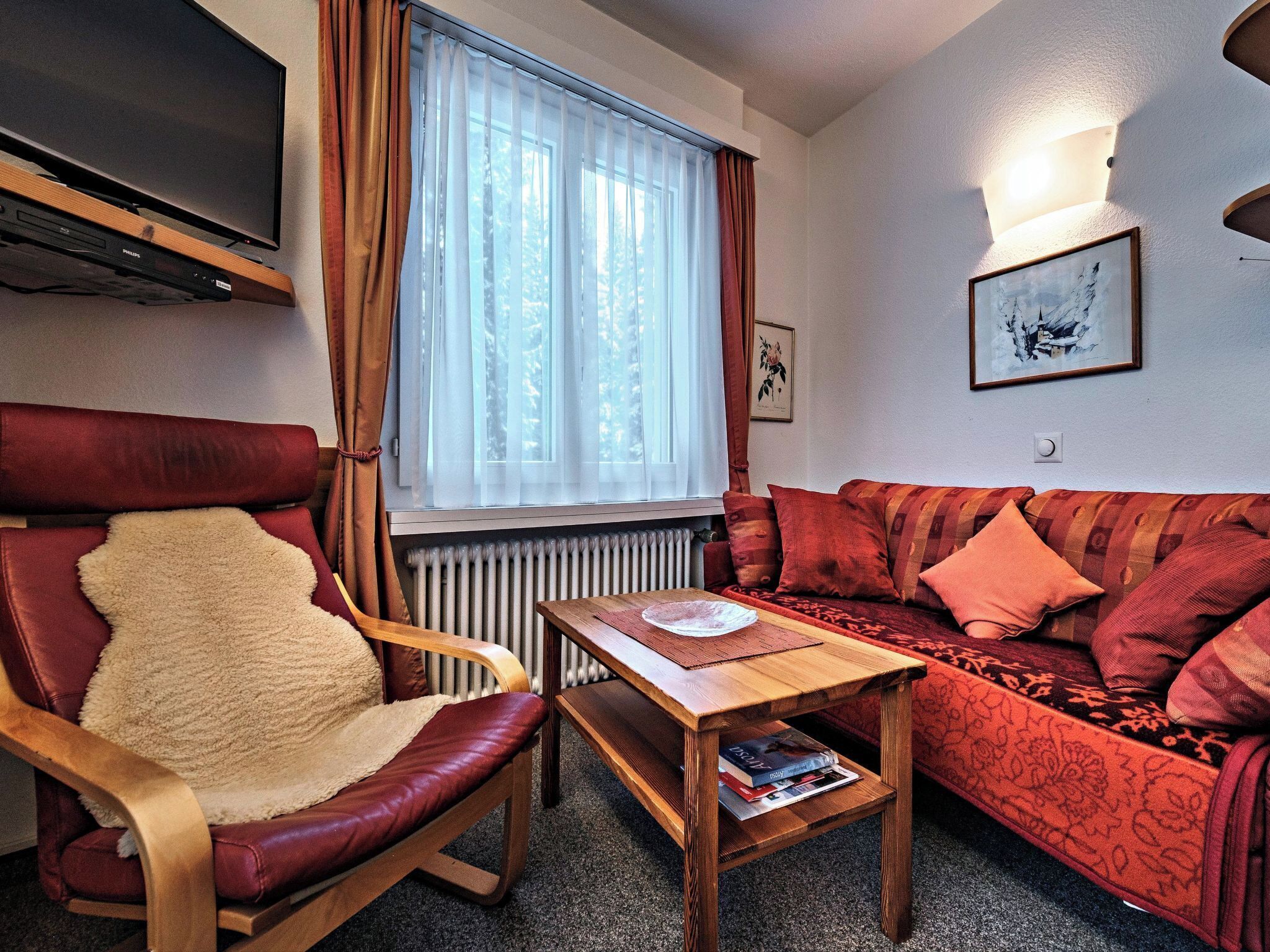 A living room with a red sofa, a wooden chair, a small wooden table, and a radiator.