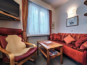 Ein Wohnzimmer mit einem roten Sofa, einem Holzstuhl, einem kleinen Holztisch und einer Heizung.