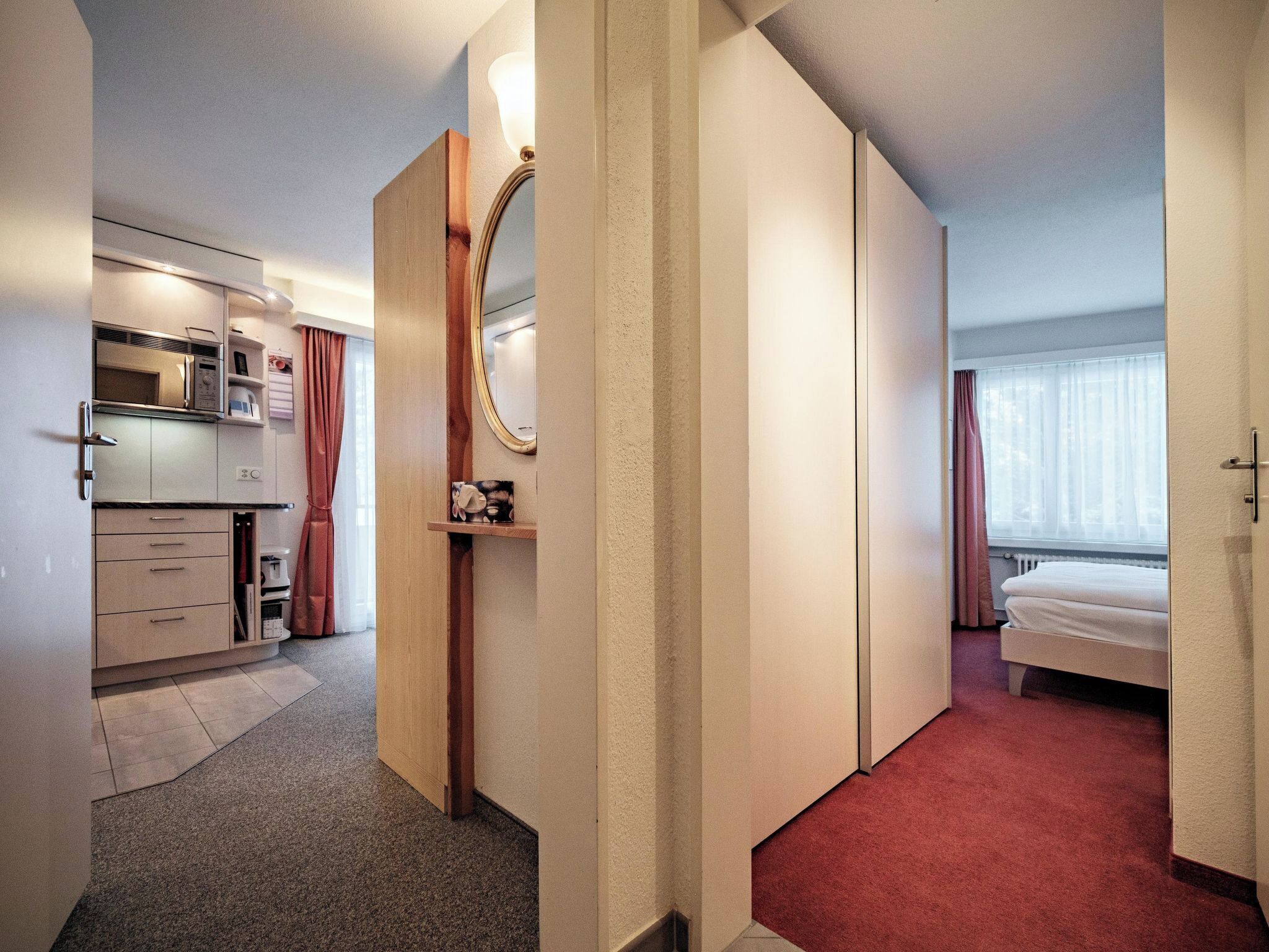 Una habitación de hotel con cama, baño, kitchenette y espejo.