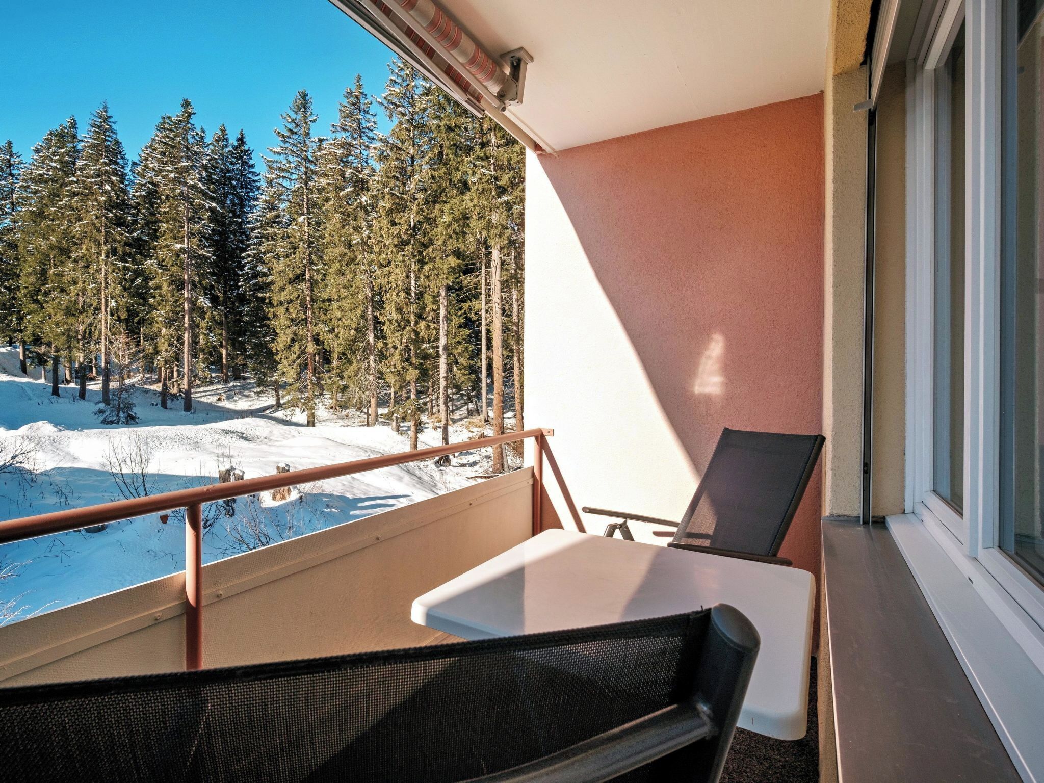 A balcony with a table and chairs, overlooking a snowy forest.