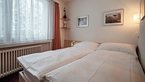 Habitación de hotel con una cama grande, un radiador, una ventana con cortinas, un florero y dos cuadros en la pared.