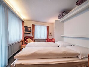 Una habitación de hotel con cama, una silla, televisión y ventana con cortinas.