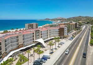 A coastal hotel with multiple floors, a parking area, and a road with vehicles. - Vista La Jolla 406A | 1BR Near Costa Azul (San José del Cabo)
