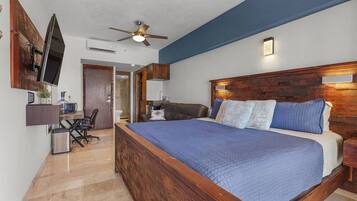 A bedroom with a large bed, a desk, a chair, a television, and a ceiling fan.