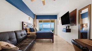 A modern bedroom with a large bed, a leather sofa, a television, and a view of the ocean. - Vista La Jolla 406B | King Suite Near Costa Azul (San José del Cabo)
