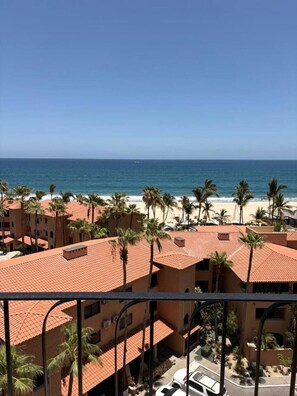 Vista de un resort frente al mar, con edificios de techos rojos, palmeras y una vista despejada del océano.