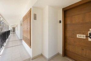 Un pasillo con una puerta de madera con la etiqueta 3415, una placa con un número en la pared y una barandilla metálica a la izquierda.