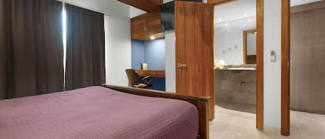 Un dormitorio con cama, escritorio y baño visible a través de una puerta abierta.