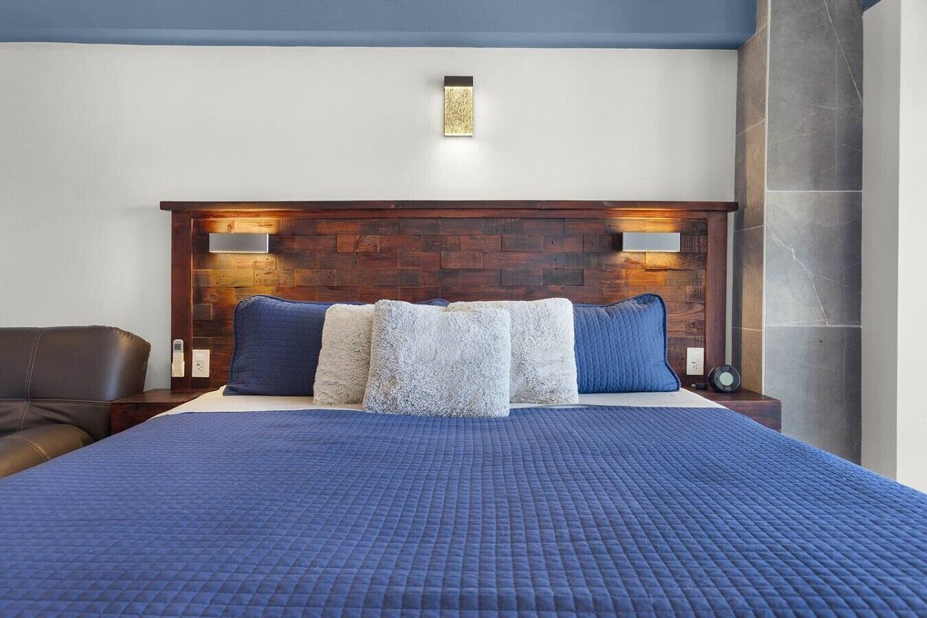 A hotel room with a large bed, a wooden headboard, two bedside lamps, and a blue bedspread.