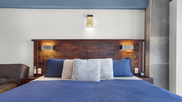 A hotel room with a large bed, a wooden headboard, two bedside lamps, and a blue bedspread. - Vista La Jolla 408B | King Suite Minutes from Costa Azul Beach (San José del Cabo)