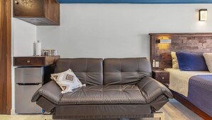 A room with a leather sofa, a bed with a headboard, a wooden cabinet, and a wall-mounted light fixture. - Vista La Jolla 408B | King Suite Minutes from Costa Azul Beach (San José del Cabo)