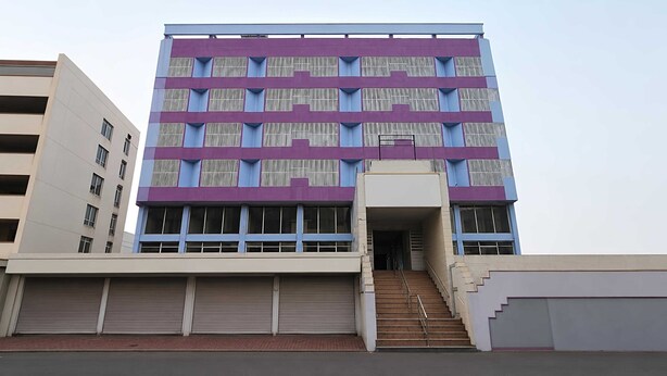 Un edificio de varios pisos con fachada morada, ventanas grandes y una escalera central que conduce a la entrada.