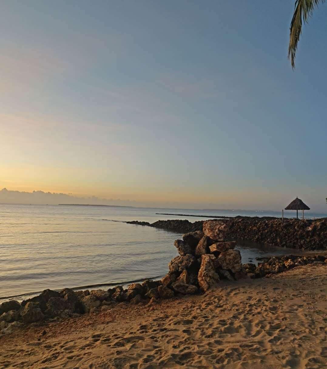 A beach with a rock formation, a thatched umbrella, and a calm sea.