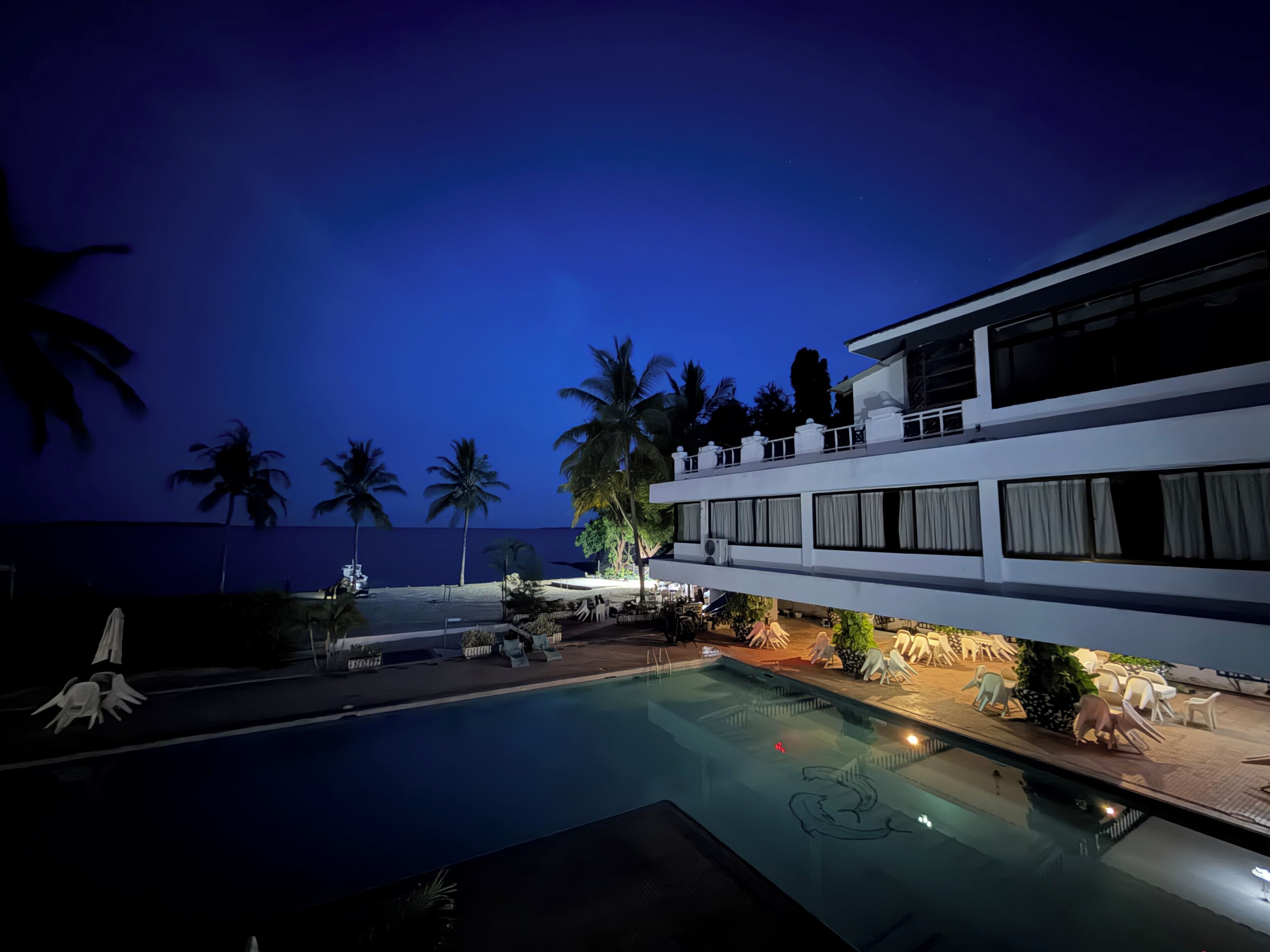 A modern building with a swimming pool, palm trees, and outdoor seating.