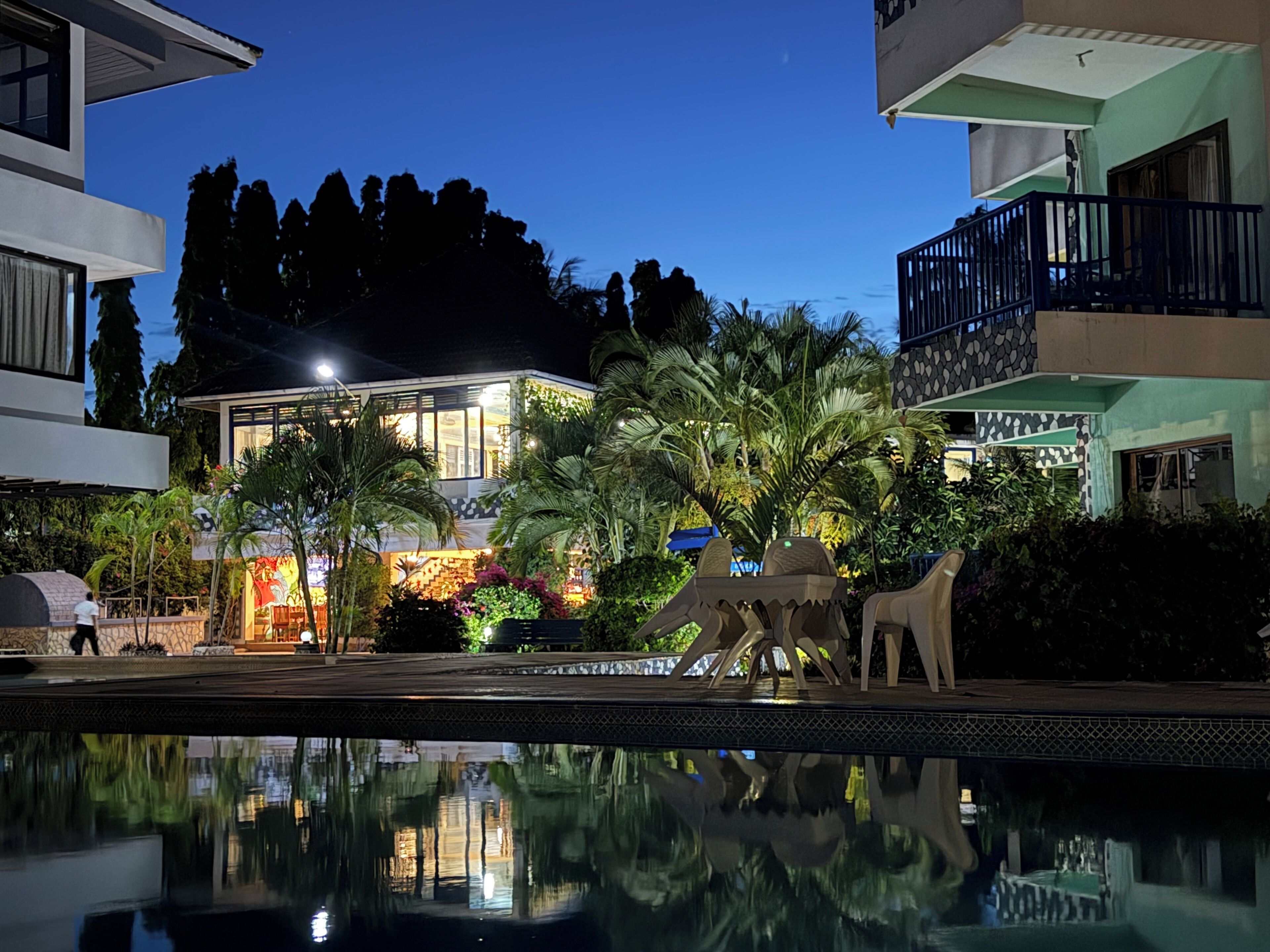 Um edifício moderno com piscina, rodeado por vegetação e palmeiras.