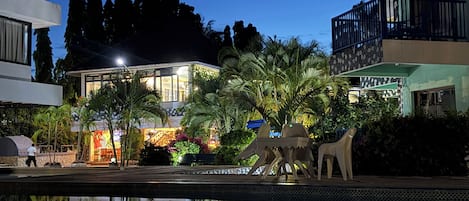 A modern building with a pool, surrounded by greenery and palm trees.