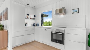 Moderni keittiö, jossa on valkoiset kaapit, Bosch-uuni ja ikkuna, josta avautuu näkymä vehreään maisemaan.