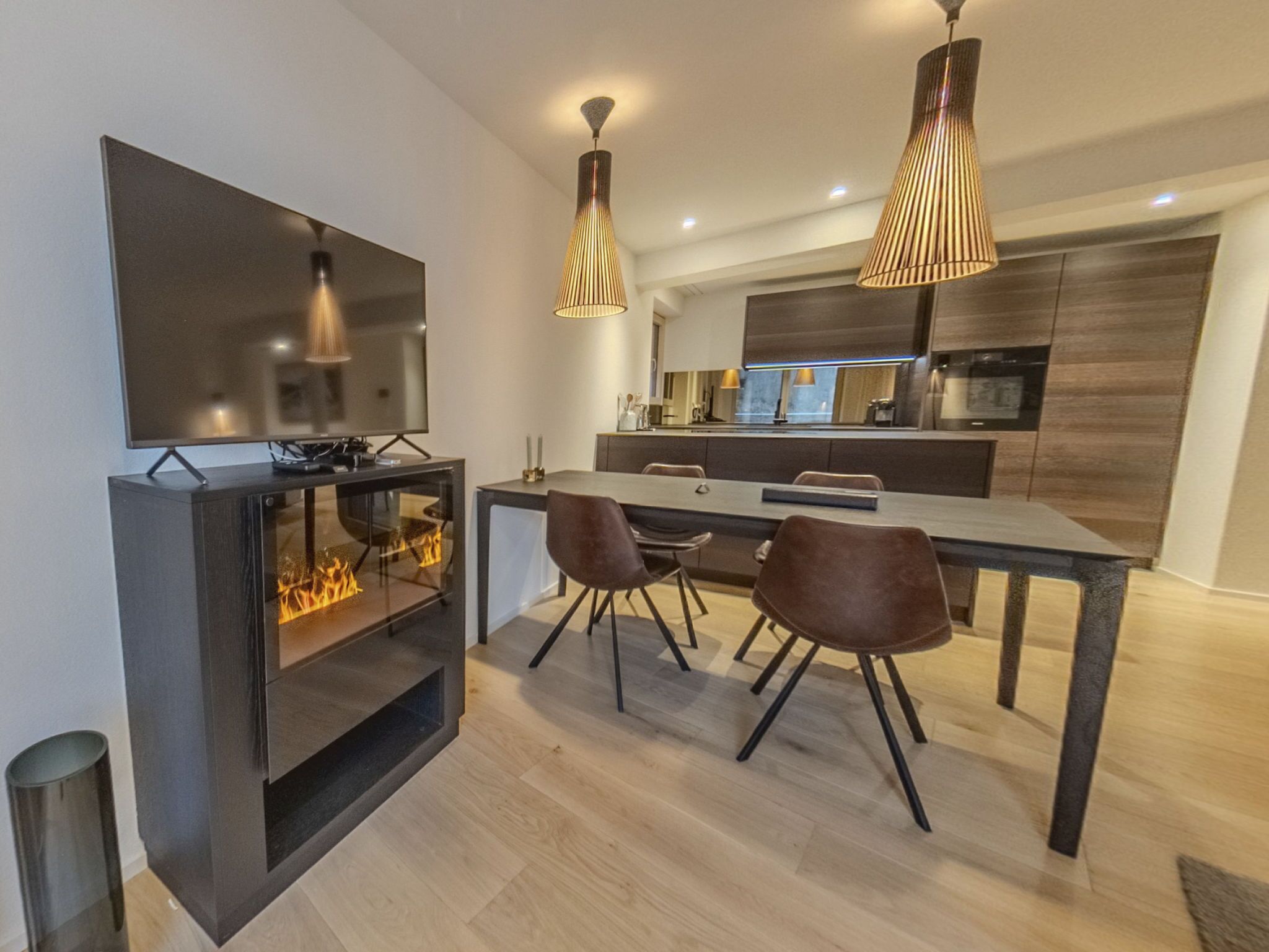 A modern kitchen with a dining area, a flat-screen TV, and a fireplace.