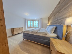 Ein Schlafzimmer mit einem Bett, einer hölzernen Kommode, einem Nachttisch und einem Fenster mit Vorhängen.