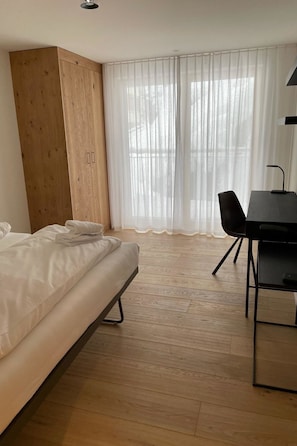 A room with a bed, a wooden wardrobe, a desk with a chair, and sheer curtains. - Koller Sapuen by Arosa Holiday Appartement/Fewo, Dusche, WC, 3-Bettwohnung by Interhome (Arosa)