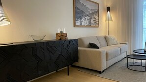Ein modernes Wohnzimmer mit einer Couch, einem schwarzen Konsolentisch, einer Glasvase und einem gerahmten Bild an der Wand.