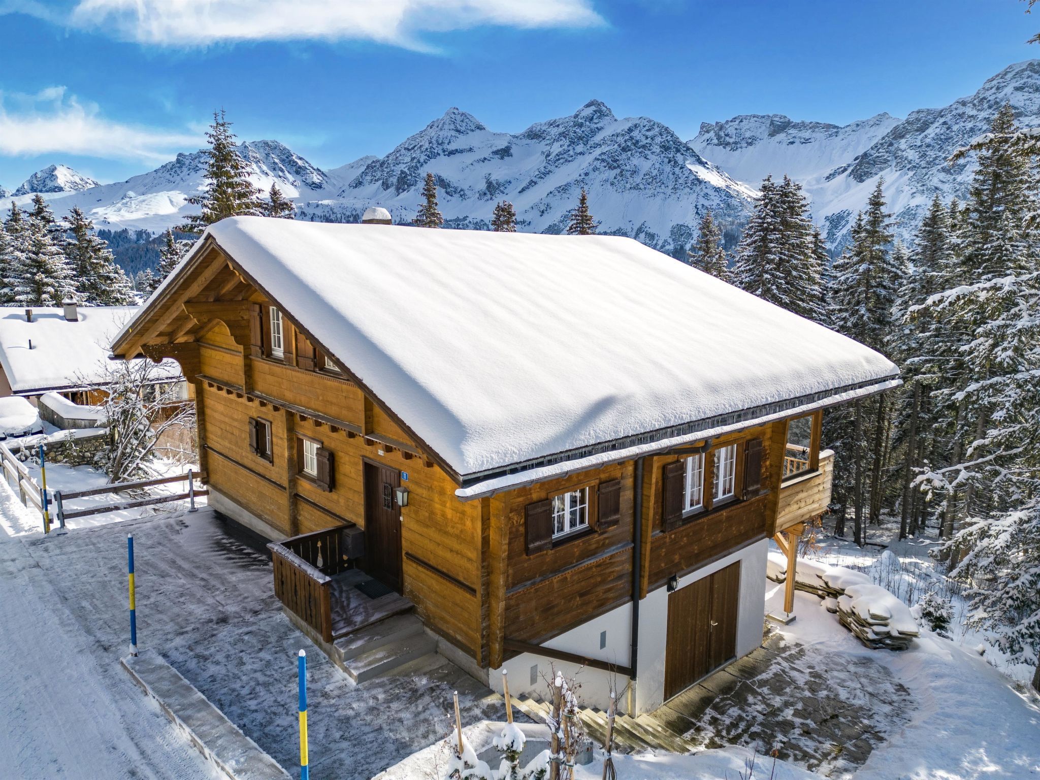 Eine Holzhütte mit verschneitem Dach, vor einer Kulisse aus schneebedeckten Bergen und Bäumen.