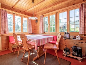 A wooden cabin with a dining area featuring a table and chairs, large windows, and a kitchenette with appliances. - Chalet Soldanella by Arosa Holiday Appartement/Fewo, Dusche oder Bad, WC, 9-Bett by Interhome (Arosa)