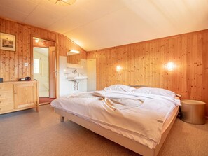 A bedroom with a wooden floor, a bed with white linens, a wooden dresser, a mirror, and a small trash bin. - Chalet Soldanella by Arosa Holiday Appartement/Fewo, Dusche oder Bad, WC, 9-Bett by Interhome (Arosa)